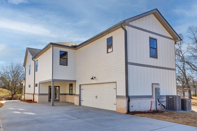 view of side of home with central AC unit, driveway, a garage, board and batten siding, and brick siding