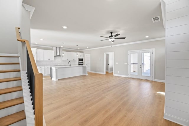 unfurnished living room featuring stairway, visible vents, ornamental molding, light wood-style floors, and french doors