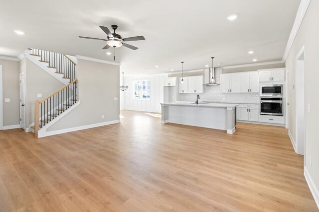 kitchen with a sink, white cabinetry, appliances with stainless steel finishes, wall chimney exhaust hood, and light countertops