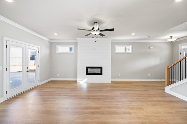 unfurnished living room featuring crown molding, light wood-type flooring, a large fireplace, and baseboards