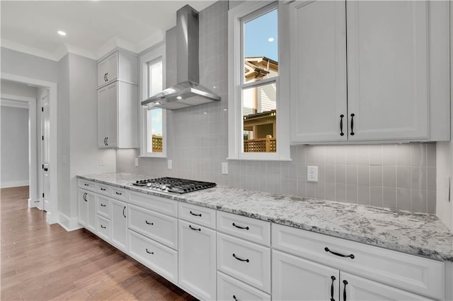 kitchen featuring wall chimney exhaust hood, white cabinetry, light hardwood / wood-style floors, backsplash, and stainless steel gas stovetop