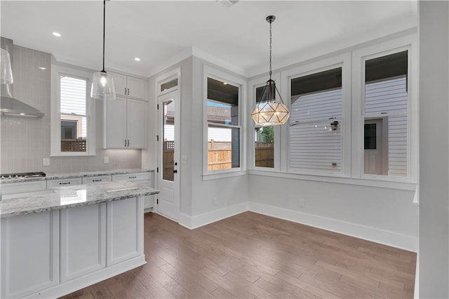 kitchen with hanging light fixtures, backsplash, light stone countertops, and white cabinetry