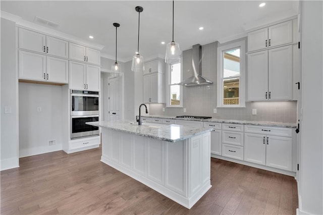 kitchen with sink, wall chimney exhaust hood, an island with sink, and white cabinetry