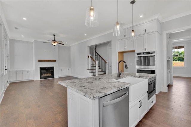 kitchen featuring white cabinets, stainless steel appliances, hanging light fixtures, a kitchen island with sink, and light stone counters
