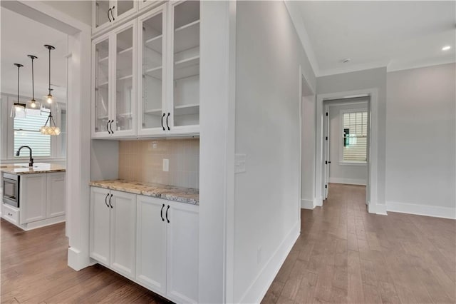 bar featuring white cabinets, decorative backsplash, light stone countertops, and hardwood / wood-style flooring