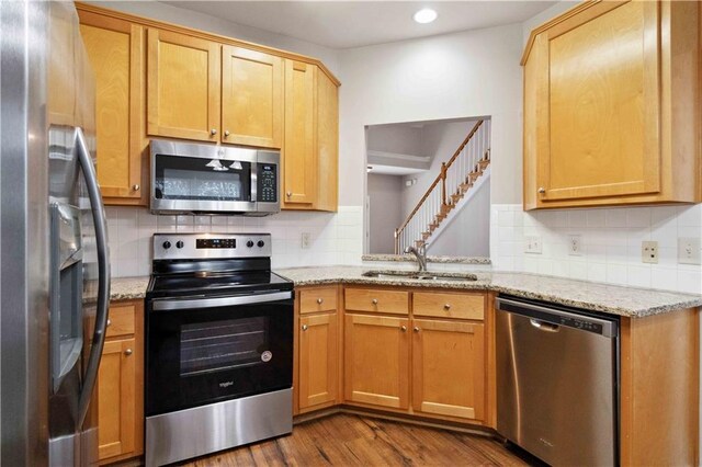 kitchen with light stone countertops, appliances with stainless steel finishes, tasteful backsplash, sink, and hardwood / wood-style flooring