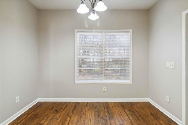 spare room with dark hardwood / wood-style floors and an inviting chandelier