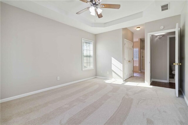 unfurnished bedroom with ceiling fan, a raised ceiling, ensuite bathroom, light colored carpet, and a closet