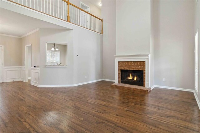 unfurnished living room featuring dark hardwood / wood-style flooring, a notable chandelier, a towering ceiling, a fireplace, and ornamental molding