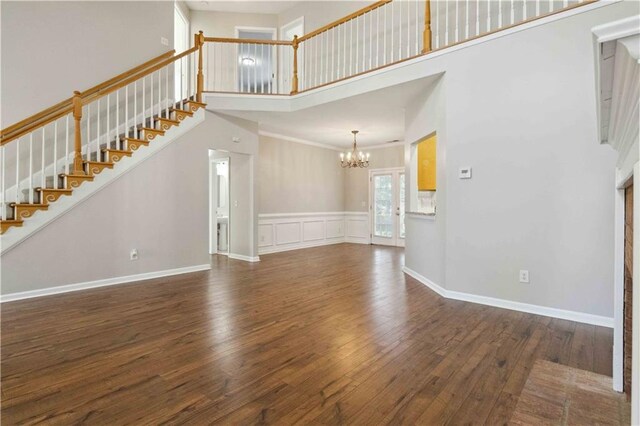 unfurnished living room with dark hardwood / wood-style flooring, a towering ceiling, and a chandelier