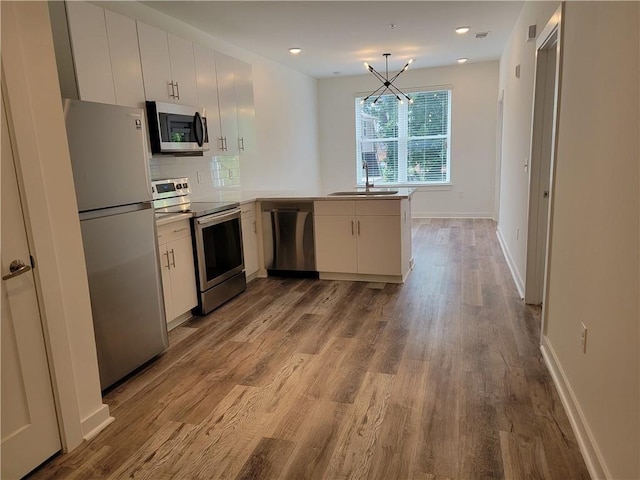 525 Parkway Dr NE Unit 306, Atlanta, GA 30308 - kitchen featuring appliances with stainless steel finishes, a peninsula, a chandelier, wood finished floors, and light countertops