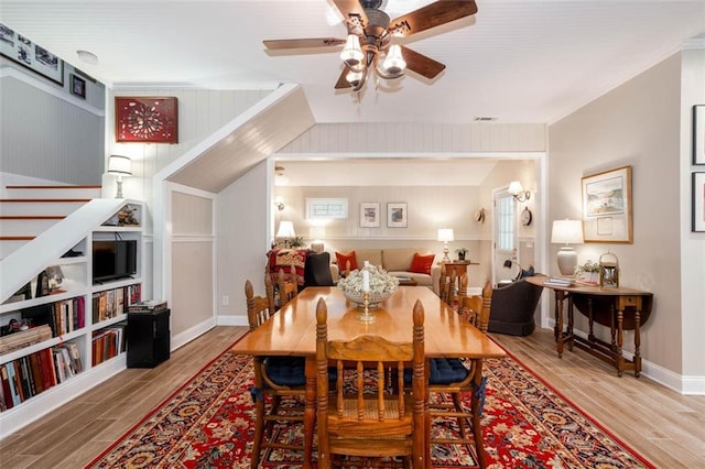 dining room with ceiling fan, ornamental molding, wood walls, and hardwood / wood-style floors