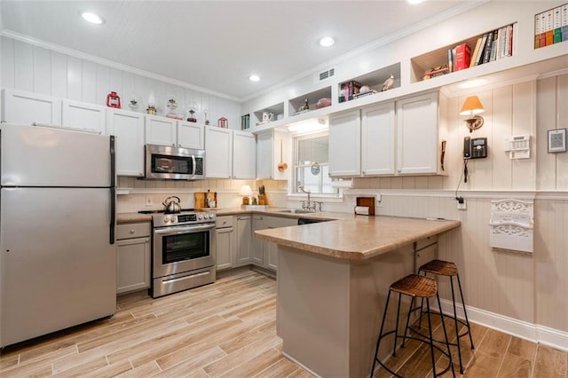 kitchen with a breakfast bar area, stainless steel appliances, ornamental molding, and white cabinetry