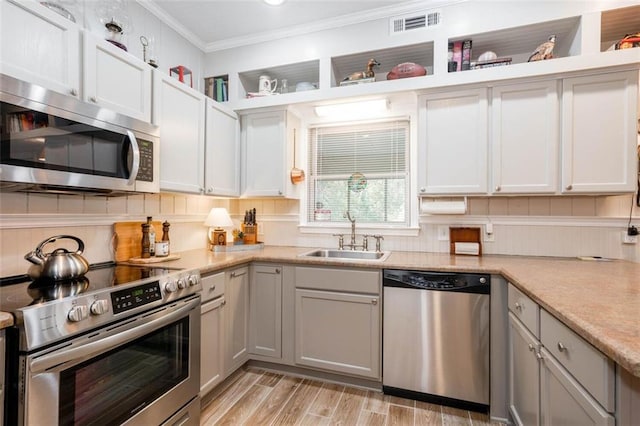 kitchen with appliances with stainless steel finishes, light hardwood / wood-style floors, white cabinets, ornamental molding, and sink