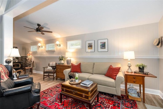 living room with a wood stove, wood walls, ceiling fan, and hardwood / wood-style floors