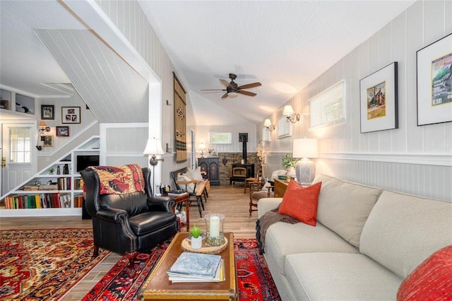 living room with ceiling fan, lofted ceiling, a wood stove, wooden walls, and hardwood / wood-style floors