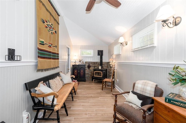 sitting room with ceiling fan, lofted ceiling, light wood-type flooring, and a wood stove