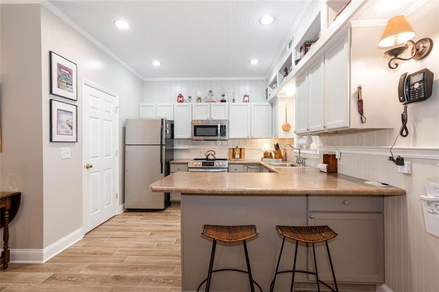 kitchen with appliances with stainless steel finishes, white cabinets, kitchen peninsula, a breakfast bar area, and sink