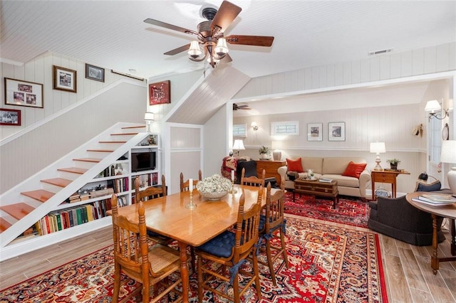 dining area with wood-type flooring, ceiling fan, and wooden walls