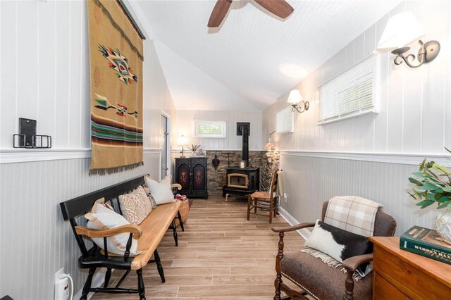 living area with a wood stove, lofted ceiling, ceiling fan, and light wood-type flooring