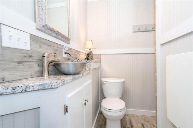 bathroom with wood-type flooring, vanity, toilet, and wood walls