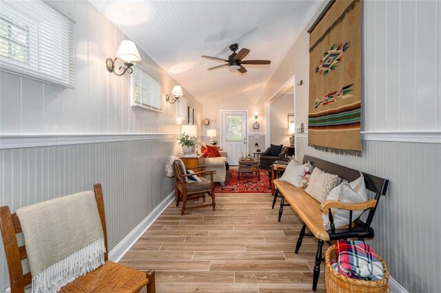 sitting room with wooden walls, vaulted ceiling, ceiling fan, and light hardwood / wood-style floors