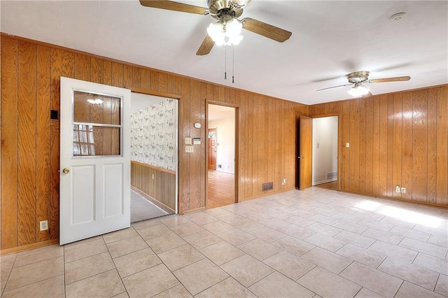 unfurnished room with ceiling fan, wooden walls, and light tile patterned floors