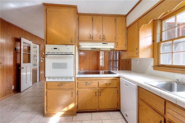 kitchen featuring tile countertops, wooden walls, decorative backsplash, light tile patterned floors, and white appliances