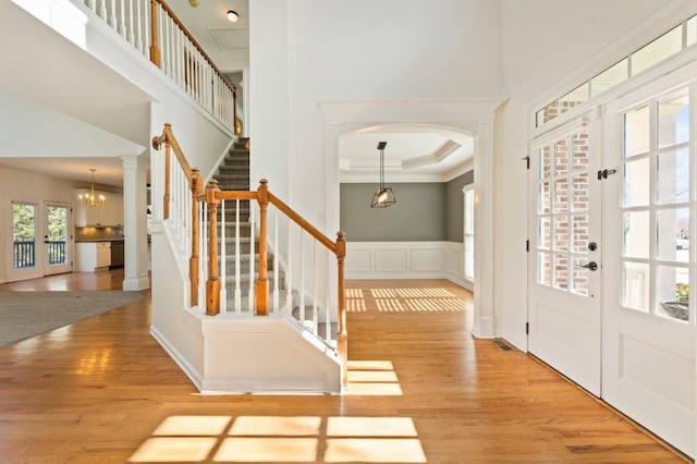 foyer entrance featuring light wood finished floors, wainscoting, a towering ceiling, stairway, and french doors