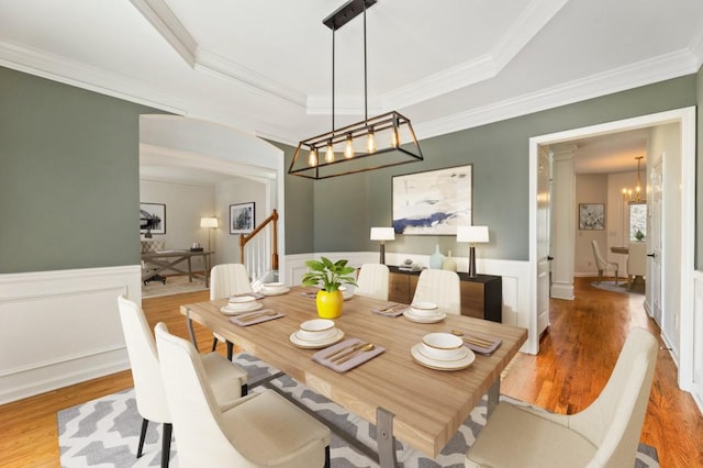 dining space with light wood-style floors, stairs, a tray ceiling, and wainscoting