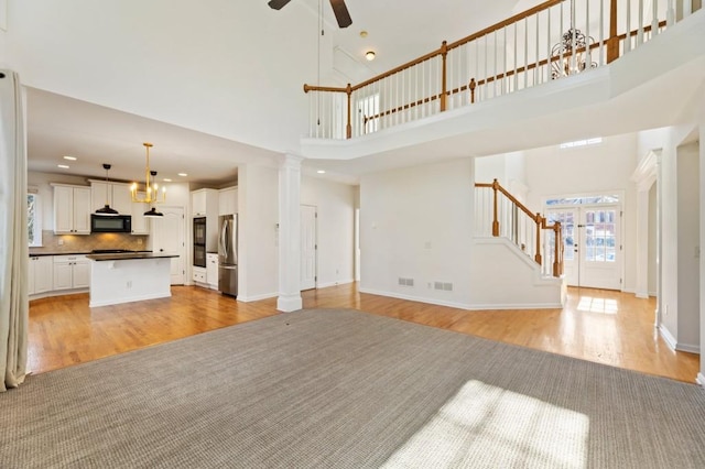 unfurnished living room with light wood finished floors, visible vents, baseboards, ceiling fan, and stairway