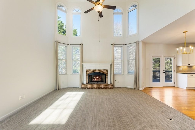 unfurnished living room featuring a healthy amount of sunlight, a fireplace, baseboards, and ceiling fan with notable chandelier