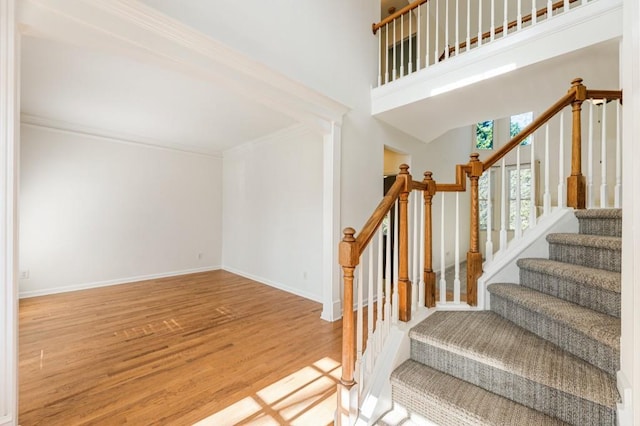 stairway with a high ceiling, baseboards, wood finished floors, and ornamental molding