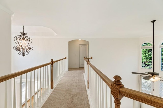 corridor with light carpet, arched walkways, a chandelier, and an upstairs landing