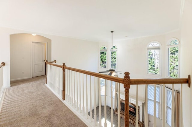 hallway featuring arched walkways, light colored carpet, and baseboards