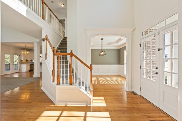 foyer entrance with wainscoting, a towering ceiling, stairway, french doors, and light wood-style floors