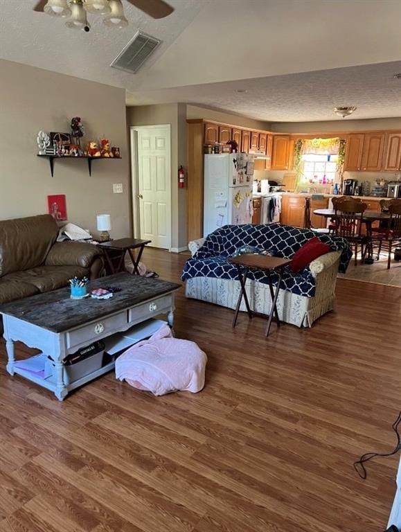 living room featuring vaulted ceiling, a ceiling fan, visible vents, and wood finished floors