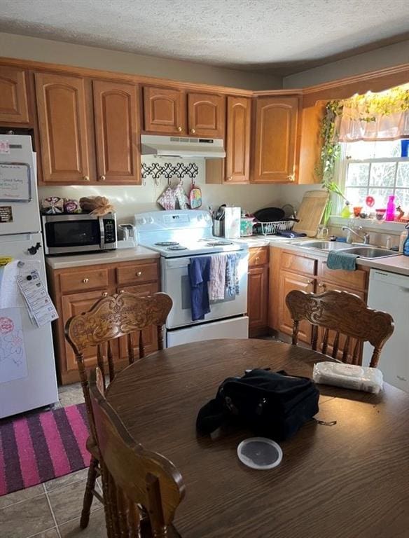 kitchen featuring a sink, white appliances, a textured ceiling, under cabinet range hood, and light countertops