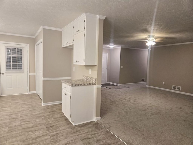 kitchen with light stone counters, light colored carpet, white cabinetry, and ornamental molding