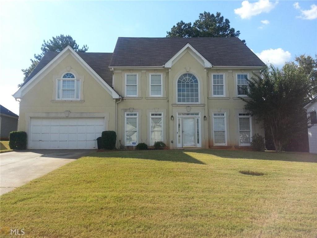 colonial home with driveway, an attached garage, a shingled roof, stucco siding, and a front lawn