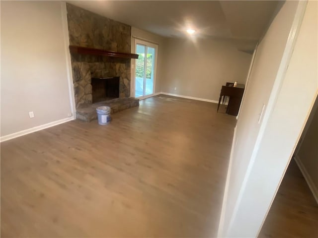 unfurnished living room with a stone fireplace and dark hardwood / wood-style floors