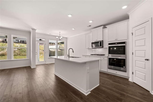 kitchen with dark wood-type flooring, an island with sink, sink, white cabinetry, and appliances with stainless steel finishes