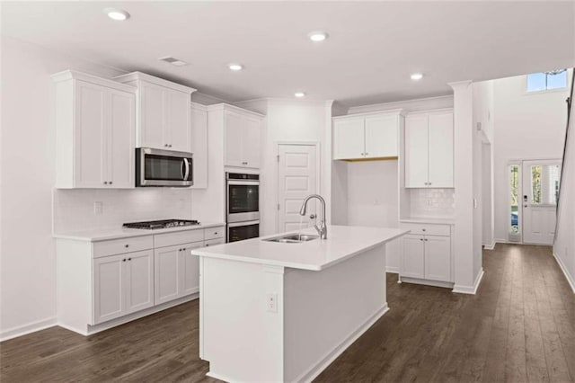 kitchen with an island with sink, white cabinetry, dark wood-type flooring, sink, and stainless steel appliances