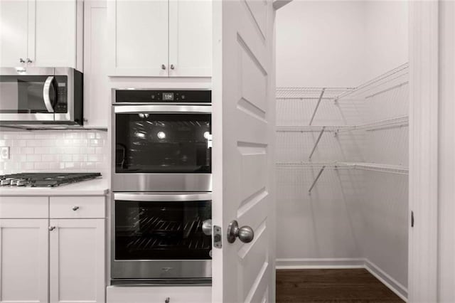 kitchen featuring dark hardwood / wood-style flooring, white cabinetry, stainless steel appliances, and backsplash