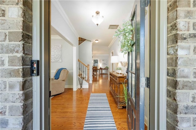 foyer entrance with crown molding, visible vents, light wood-type flooring, baseboards, and stairs