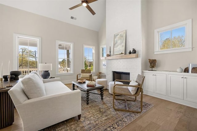 sitting room with ceiling fan, high vaulted ceiling, a fireplace, wood finished floors, and visible vents