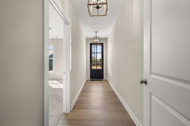 doorway featuring a notable chandelier, baseboards, and wood finished floors