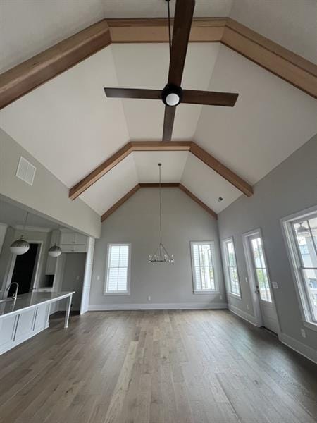 unfurnished living room featuring high vaulted ceiling, a notable chandelier, baseboards, and wood finished floors