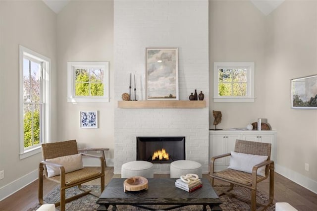 living area featuring baseboards, dark wood-style flooring, plenty of natural light, and a brick fireplace