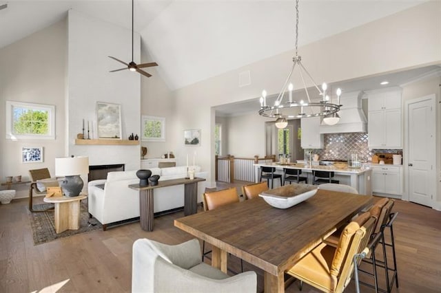 dining space with a healthy amount of sunlight, high vaulted ceiling, wood finished floors, and ceiling fan with notable chandelier